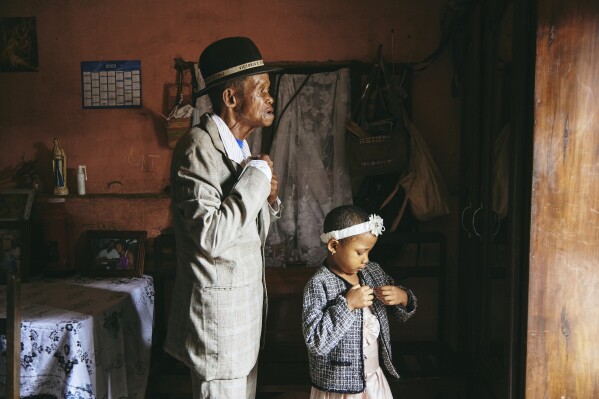 This image provided by World Press Photo and taken by Lee-Ann Olwage for GEO is part of a series titled Valim-babena which won the World Press Photo Story of the Year Award and shows Dada Paul Rakotazandriny (91), who is living with dementia, and his granddaughter, Odliatemix Rafaraniriana (5), get ready for church on Sunday morning at his home in Antananarivo, Madagascar. 12 March 2023. (Lee-Ann Olwage/Geo/World Press Photo via AP)