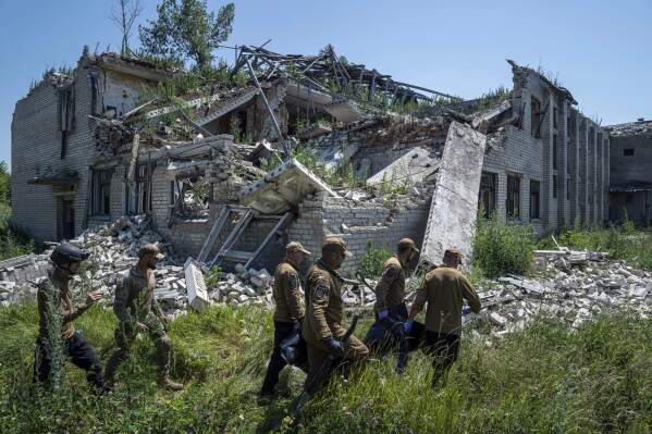 FILE - Oleksii Yukov, second right, and other body collectors carry the body of a Russian soldier that was exhumed from a shell crater in front of destroyed school in Virnopillia, Ukraine, Thursday, July 6, 2023. (AP Photo/Evgeniy Maloletka, File)