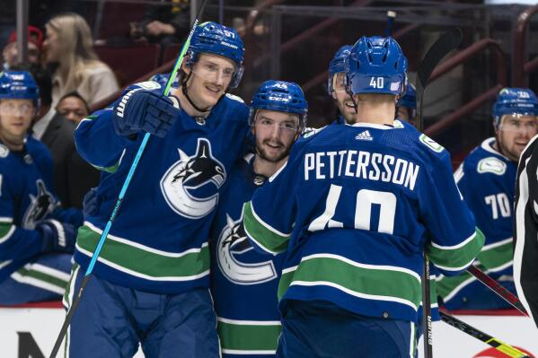 Vancouver Canucks' Kyle Burroughs, middle, celebrates with Tyler Myers, left, and Elias Pettersson after scoring a goal against the Winnipeg Jets during the second period of an NHL hockey game Friday, Nov. 19, 2021, in Vancouver, British Columbia. (Rich Lam/The Canadian Press via AP)