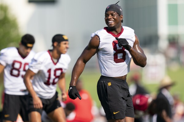 FILE - Washington Commanders running back Brian Robinson Jr. laughs while warming up during an NFL football practice at the team's training facility, Friday, July 28, 2023, in Ashburn, Va. Brian Robinson Jr. was shot twice in the right leg a year ago in an attempted robbery/carjacking in Washington. He made his NFL debut for the Commanders six weeks later and ran for nearly 800 yards in his first 12 professional games. That was an impressive rookie season for third-round pick out of Alabama. But now Robinson says he feels a night and day difference from where he was last year. (AP Photo/Stephanie Scarbrough, File)