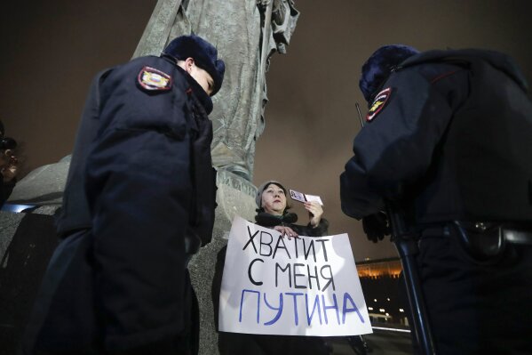Police officers check a protester's ID as she holds a poster that reads: "Enough Putin for me" while taking part in a one-man protest in front of the monument of the Prince Vladimir next to the Kremlin in Moscow, Russia, Wednesday, March 11, 2020. The constitutional reform passed by the Duma on Wednesday would allow Putin to run for presidency two more times after 2024. Before the national vote, it will be reviewed by Russia's Constitutional Court. (AP Photo/Pavel Golovkin)