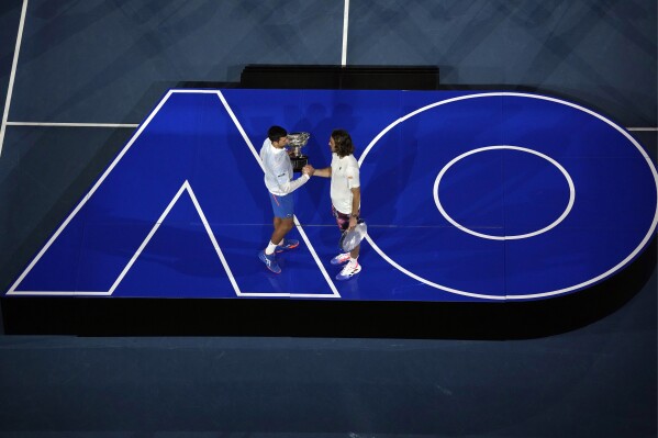 FILE - Novak Djokovic of Serbia, left, greets Stefanos Tsitsipas of Greece as he holds the Norman Brookes Challenge Cup after defeating Tsitsipas in the men's singles final at the Australian Open tennis championship in Melbourne, Australia, Sunday, Jan. 29, 2023. The 2024 Australian Open, the year's first Grand Slam tennis tournament, begins at Melbourne Park on Sunday morning (Saturday night ET). That's a day earlier than usual, creating a 15-day event for the first time. (AP Photo/Ng Han Guan, File)