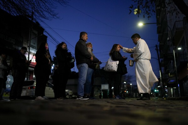 A priest blesses those visiting the Church of San Cayetano, the patron Saint of work, on his feast day in Buenos Aires, Argentina, early Monday, Aug. 7, 2023. (AP Photo/Natacha Pisarenko)