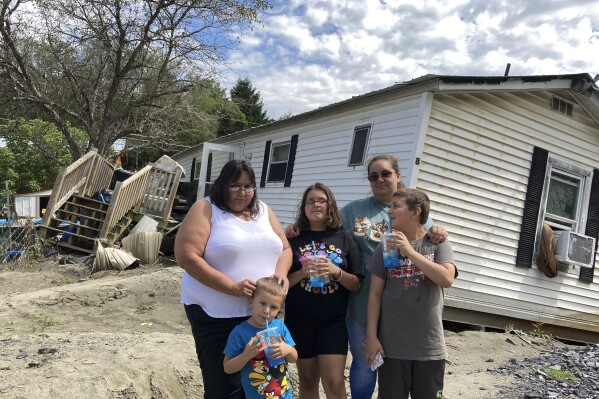 Sara Morris and her children stand outside their flood-ravaged mobile home in Berlin, Vt., on Tuesday, Aug. 29, 2023. With Vermont’s already tight housing market and cold weather fast approaching, some flood victims who lost homes don’t yet know where they’ll live. (AP Photo/Lisa Rathke)