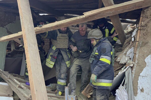 In this photo provided by the Ukrainian Emergency Service, emergency workers help a wounded man after a residential houses were badly damaged in a Russian missile attack, near Kryvyi Rih, Ukraine, Monday, Jan. 8, 2024. (Ukrainian Emergency Service via AP)