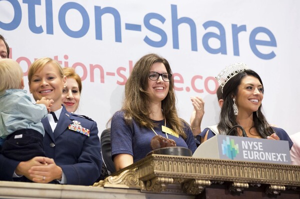 In this photo provided by the New York Stock Exchange, Adoption-Share founder and CEO Thea Ramirez, center, Miss Utah USA 2013 Marissa Powell, right, and fellow adoption supporters ring the opening bell at the New York Stock Exchange in New York on Aug. 20, 2013. Ramirez has overstated the capabilities of her proprietary Family-Match algorithm to government officials as she seeks to expand its reach nationwide, even as social workers told AP in 2023, that the tool wasn’t useful and often led them to unwilling families. (NYSE via AP)