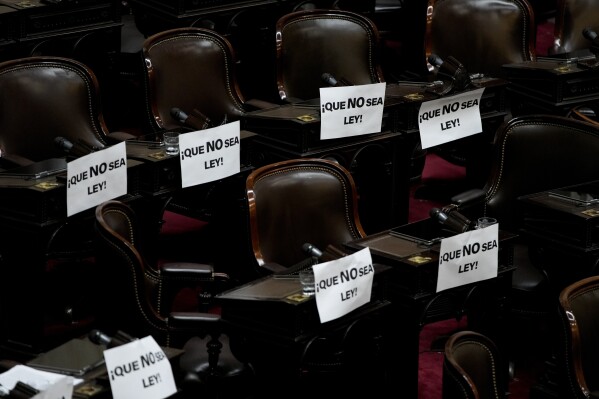 Signs with a message that read in Spanish: "let it now be a law", are attached to lawmakers' desks at the end of a session where a bill promoted by Argentine President Javier Milei was approved in general by the lower house of Congress, in Buenos Aires, Argentina, Friday, Feb. 2, 2024. The bill, that includes a broad range of economic, administrative, criminal and environmental reforms, must now be debated article by article and will then be sent to the Senate. (AP Photo/Natacha Pisarenko)