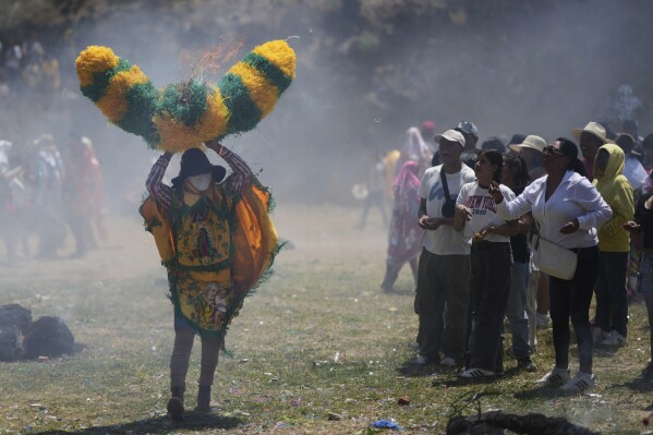 Onlookers throw lit matches at a reveler, known as a sayon, wielding a tissue paper hat during Easter celebrations in Tetela del Volcan, Mexico, Sunday, April 20, 2025. (AP Photo/Eduardo Verdugo)
