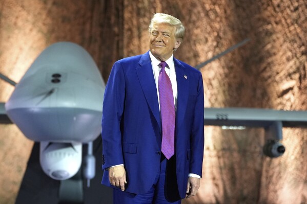 President Donald Trump smiles backdropped by an MQ-9 Reaper drone before addressing military personnel at the Al Udeid Air Base, Thursday, May 15, 2025, in Doha, Qatar. (AP Photo/Alex Brandon)