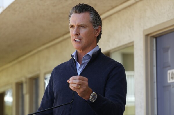 FILE - California Gov. Gavin Newsom gives an update on the state's initiative to provide housing for homeless Californians to help stem the coronavirus, during a visit to a Motel 6 participating in the program in Pittsburg, Calif., June 30, 2020. California cities and counties still don't know how much they'll have to pay for Newsom's pandemic program to house homeless people in hotel rooms after the Federal Emergency Management Agency said in October 2023 that it was limiting the number of days eligible for reimbursement. (AP Photo/Rich Pedroncelli, Pool)