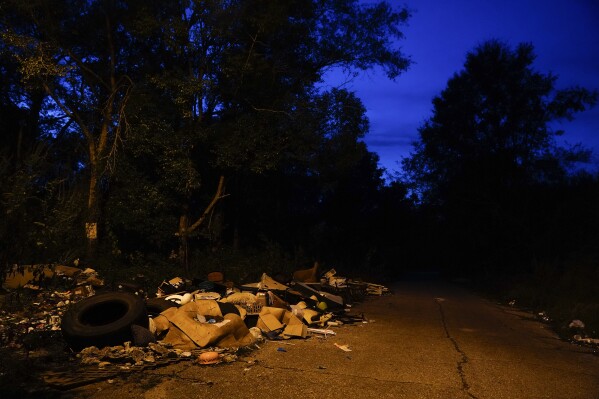 A street light illuminates garbage and old tires covering a street that leads to Angela Adams' home on Tuesday, Dec. 5, 2023, in Prichard, Ala. Adams drives around potholes, past mounds of household debris and abandoned houses and sometimes through flooded streets to reach her home of 30 years in Prichard's Alabama Village, where almost one-fifth of the city’s drinking water is lost through leaky pipes. (AP Photo/Brynn Anderson)