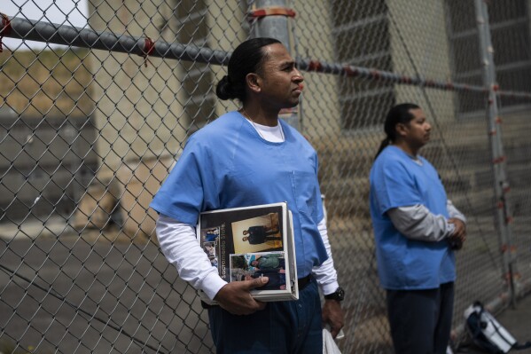 Gerald Massey, an incarcerated student majoring communications through the Transforming Outcomes Project at Sacramento State (TOPSS), holds a binder with his family photos while waiting for his class to start at Folsom State Prison in Folsom, Calif., Wednesday, May 3, 2023. Born in San Francisco to parents who immigrated to the U.S. from Pakistan, Massey recalls growing up feeling like an outsider. (AP Photo/Jae C. Hong)