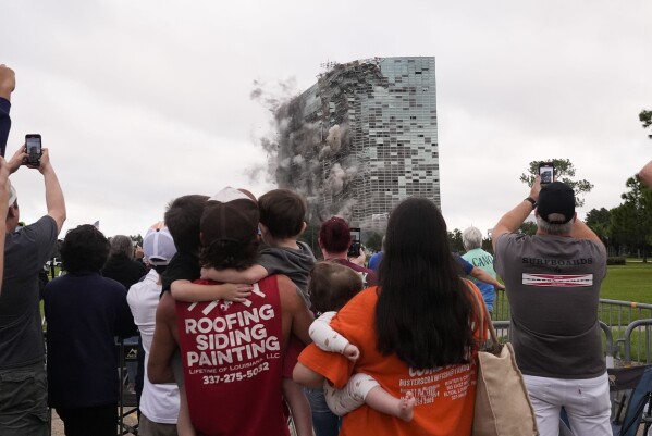 Tuff Gary, left, and Morgan LeBlanc with their children Hudson, Tuff, Jr., and Zander, of Jenning, La., watch the implosion of the Hertz Tower, that was heavily damaged after Hurricanes Laura and Delta in 2020, in Lake Charles, La., Saturday, Sept. 7, 2024. (AP Photo/Gerald Herbert)