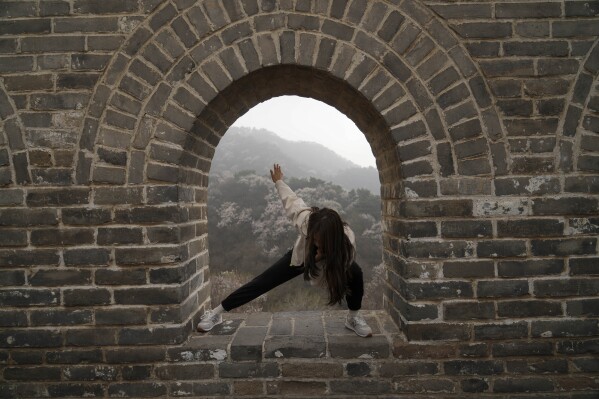 A woman poses for photos on the window of a watch tower along the Badaling section of the Great Wall of China on the outskirts of Beijing, Saturday, April 13, 2024. (AP Photo/Tatan Syuflana)