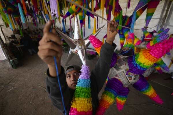 A worker hangs the most traditional style of "piñata," a sphere with seven spiky cones, that will be filled with fruit and candy at a family-run piñata-making business in Acolman, just north of Mexico City, Wednesday, Dec. 13, 2023. This style of piñata has a religious origin, with each cone representing one of the seven deadly sins, and hitting the globe with a stick is a symbolic blow against sin. (AP Photo/Fernando Llano)