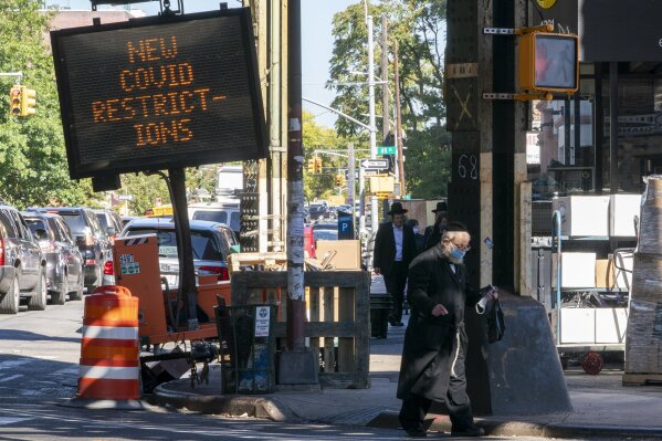 A traffic sign warns of new COVID-19 restrictions on New Utrecht Ave. in the Orthodox Jewish neighborhood of Borough Park in the Brooklyn borough of New York, Wednesday, Oct. 14, 2020. New York Gov. Andrew Cuomo threatened Wednesday to take away state funding from schools in coronavirus hot spots that are ignoring orders to shut their doors. The action came amid news reports on Jewish religious schools staying open in defiance of the rules in some parts of Brooklyn and Orange County. (AP Photo/Mary Altaffer)