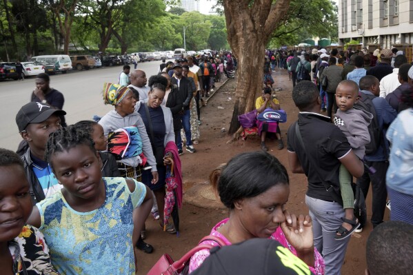 Travelers are seen in a queue outside the passport offices in Harare, Wednesday, Dec. 20, 2023. Atop many Christmas wish lists in economically troubled Zimbabwe is a travel document and people are flooding the passport office this holiday season ahead of a price hike planned in the New Year. The desperation at the office in the capital is palpable as some people fear the hike could push the cost of obtaining a passport out of reach and economic gloom feeds a surge in migration. (AP Photo/Tsvangirayi Mukwazhi)