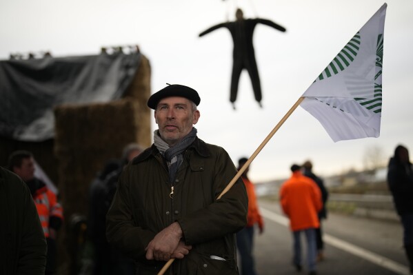 A farmer stands at a barricade as farmers block a highway Tuesday, Jan. 30, 2024 in Jossigny, east of Paris. With protesting farmers camped out at barricades around Paris, France's government hoped to calm their anger with more concessions Tuesday to their complaints that growing and rearing food has become too difficult and not sufficiently lucrative. (AP Photo/Christophe Ena)