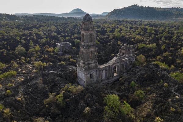 A church tower peeks above from where lava from the Paricutin volcano buried the church decades ago, in San Juan Parangaricutiro, Mexico, Tuesday, Feb. 21, 2023. Paricutin’s lava eventually covered seven square miles (18.5 square kilometers). Its slow advance allowed residents of the surrounding communities to relocate to land donated by the government. (AP Photo/Eduardo Verdugo)