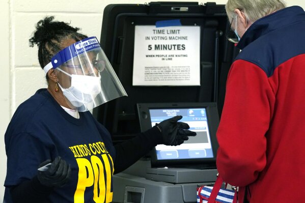 FILE - In this Nov. 3, 2020, file photo, Precinct 36 poll worker Vivian Bibens wears personal protective equipment as she explains the purpose of the ballot scanner to a voter on Election Day in Jackson, Miss. The 2020 presidential election had all the makings of a looming disaster: fears of Russian meddling, violence at the polls, voter intimidation and poll workers fleeing their posts over the coronavirus. But the election was largely smooth, in large part because 107 million voters that cast their ballots early and took the pressure off Election Day operations. (AP Photo/Rogelio V. Solis, File)