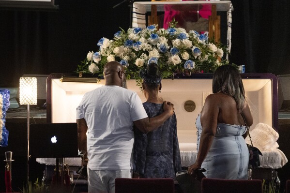 FILE — O'Shae Sibley's father Jake Kelly, left, mother Onetha Sibley, center, and stepmother Jacqueline Kelly gather by the casket during a celebration of life for O'Shae Sibley Aug. 8, 2023, at The Met Philadelphia, in Philadelphia. A 17-year-old has been indicted on a hate-crime murder charge in a stabbing that followed taunts and confrontation over a group of men dancing shirtless to Beyoncé as they gassed up their car, prosecutors said Thursday, Aug 10, 2023, in New York. (AP Photo/Joe Lamberti, File)