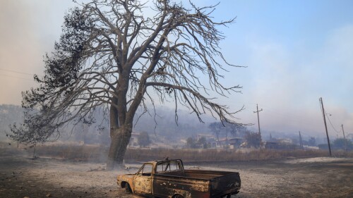 A damaged car stands in front of a burned tree near Loutraki 80 Kilometres west of Athens, Greece, Monday, July 17, 2023. Two wildfires threatened homes in areas outside Athens, where strong winds made the flames difficult to contain. Most of southern Greece, including greater Athens, was an elevated level of alert for fire risk, while more extreme temperatures are expected later this week. (AP Photo/Petros Giannakouris)
