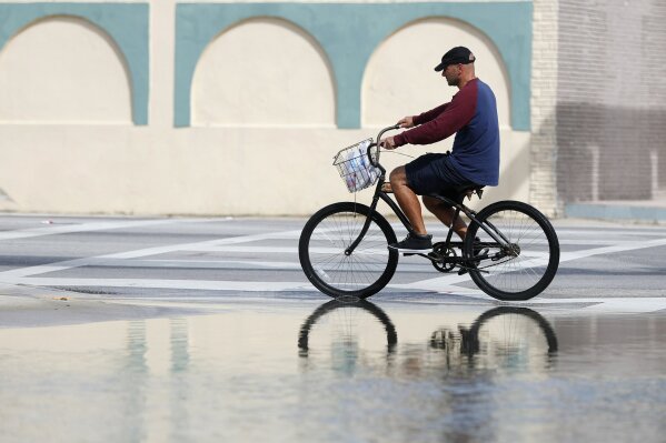 FILE - In this Oct. 9, 2018, file photo, a cyclist rides past an area flooded during a King Tide, an especially high tide, in Miami. Federal scientists, according to a report released Wednesday, July 10, 2019,  predict 40 places in the U.S. will experience higher than normal rates of so-called sunny day flooding this year due to rising sea levels and an abnormal El Nino weather system. (AP Photo/Wilfredo Lee, FIle)