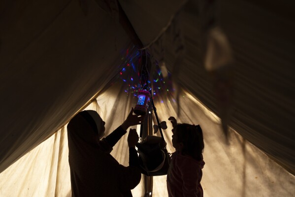 Randa Baker, who was displaced by the Israeli bombardment of the Gaza Strip, hangs Ramadan decorations and lanterns with her daughter, remarking the beginning of the Muslim holy fasting month of Ramadan at a makeshift tent camp in the Muwasi area, southern Gaza, March 11, 2024. The holy month, typically a time of communal joy and reflection, is overshadowed by the grim reality of a conflict that has claimed over 30,000 Palestinian lives and left vast swaths of Gaza in shambles. (AP Photo/Fatima Shbair)