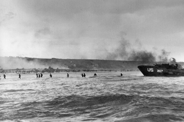 FILE - Under the cover of naval shell fire, American infantrymen wade ashore from their landing craft during the initial Normandy landing operations in France, June 6, 1944. More than 2,200 Allied aircraft begin bombing German defenses and other targets in Normandy. They are followed by 1,200 aircraft carrying more than 23,000 American, British and Canadian airborne troops. British forces landing in gliders take two strategic bridges near the city of Caen. (AP Photo/Peter Carroll, File)