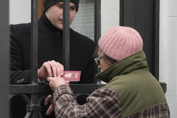 A Russian Embassy security guard checks the passport of a Russian woman who queued at the Russian Embassy in Warsaw, Poland, Sunday, March 17, 2024 to cast her vote on the last day of the three-day presidential elections. Russians at home and abroad headed to the polls for a presidential election that was all but certain to extend President Vladimir Putin's rule after he clamped down on dissent. (AP Photo/Czarek Sokolowski)