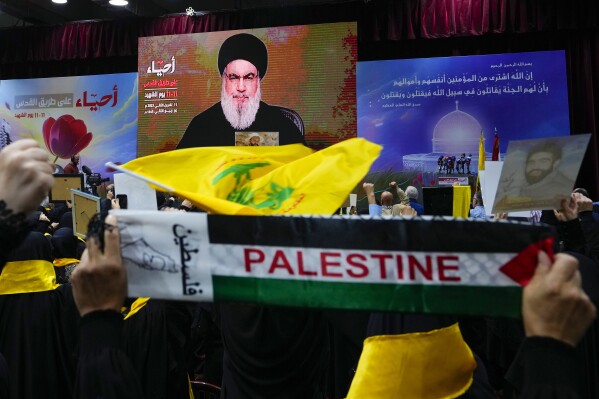 Supporters of the Iranian-backed Hezbollah group raise their fists in salute as they listen to a speech by Hezbollah leader Sayyed Hassan Nasrallah via video link, during a ceremony marking the "Hezbollah Martyr Day," in the southern Beirut suburb of Dahiyeh, Lebanon, Saturday, Nov. 11, 2023. (AP Photo/Hassan Ammar)