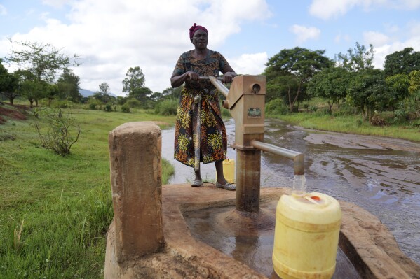 Rhoda Peter enche recipientes com água de uma barragem de areia no condado de Makueni, Quênia, na sexta-feira, 1º de março de 2024. Ela estava buscando água para limpar utensílios e lavar roupas. (Foto AP/Brian Inganga)