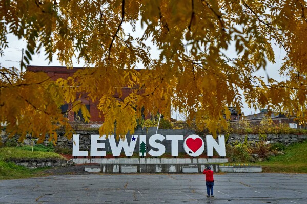 A man photographs a make-shift memorial at the base of the Lewiston sign at Veteran's Memorial Park, Sunday, Oct. 29, 2023, in Lewiston, Maine. The community is working to heal following shooting deaths of 18 people at a bowling alley and a bar in Lewiston on Wednesday, Oct. 25. (AP Photo/Matt York)