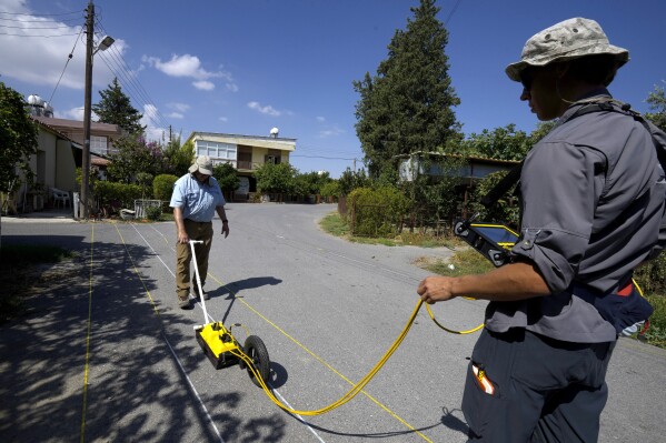 Harry M. Jol, left, a geography and anthropology professor at the University of Wisconsin Eau Claire, and his son Connor, right, operate a ground-penetrating radar in the village of Exo Metochi, Duzova, in the Turkish occupied area at breakaway Turkish Cypriot north of ethnically divided Cyprus on Tuesday, Sept. 5, 2023. Emitting radio waves, the machine is probing for any disturbances through layers of soil beneath the asphalt to offer any clues supporting eyewitness accounts that people who vanished nearly a half century ago are buried in a makeshift mass grave, now squeezed between a two-story home and a fig orchard. (AP Photo/Petros Karadjias)