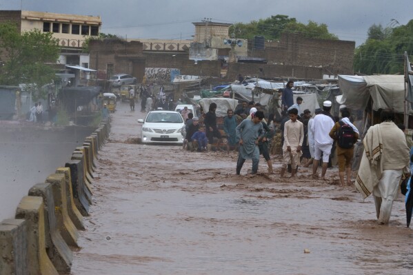 People wade through a flooded bridge on a stream, which is overflowing following heavy rains, on the outskirts of Peshawar, Pakistan, Monday, April 15, 2024. Lightnings and heavy rains killed dozens of people, mostly farmers, across Pakistan in the past three days, officials said Monday, as authorities declared a state of emergency in the country's southwest following an overnight rainfall to avoid any further casualties and damages. (AP Photo/Muhammad Sajjad)