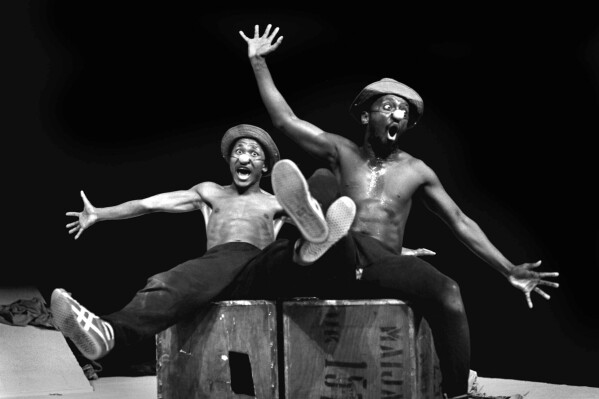 FILE — Performers Percy Mtwa, left, and Mbongeni Ngema in a scene from "Woza Albert" at the Market Theatre in Johannesburg, South Africa, in 1981. Ngema, enowned South African playwright, producer and composer has died in a fatal car crash at the age of 68, his family confirmed on Wednesday, Dec. 27, 2023. (AP Photo/Ruphin Coudyzer/File)