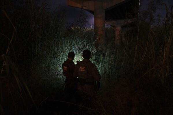 Andrés García, left, and Christina Smallwood, Border Patrol agents and Public Affairs officers, look for migrants underneath the vehicular McAllen-Hidalgo International Bridge in Hidalgo, Texas, early Friday, Aug. 9, 2024. (Verónica Gabriela Cárdenas/The Texas Tribune via AP)
