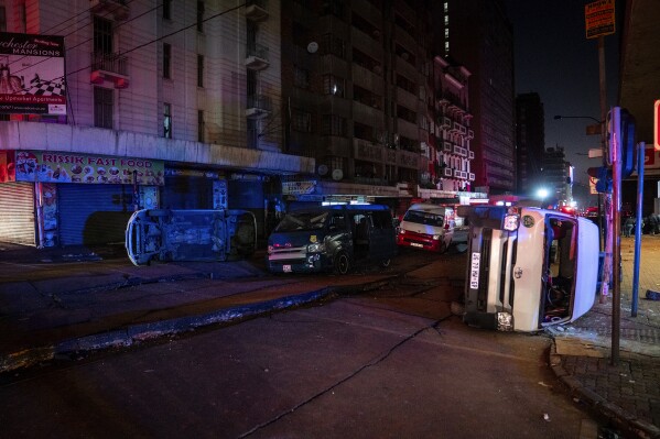 Minibus taxis lie on their side after being blown at the scene of a gas explosion downtown Johannesburg, South Africa, Wednesday July 19, 2023. Search and rescue officials also ordered residents in nearby buildings to evacuate the area and the area where the explosion happened was cordoned off. (AP Photo/Shiraaz Mohamed)