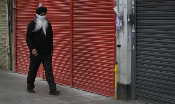 A man wearing a mask to protect against coronavirus, walks past shuttered shops on a usually bustling high street as the country continues its lockdown to help curb the spread of the virus, in London, Monday, April 27, 2020. While Britain is still in lockdown, some nations have begun gradually easing coronavirus lockdowns, each pursuing its own approach but all with a common goal in mind, restarting their economies without triggering a new wave of infections. (AP Photo/Kirsty Wigglesworth)