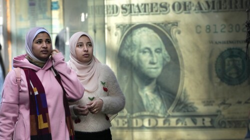 FILE - Egyptians walk past a poster depicting a US dollar outside an exchange office in Cairo, Egypt, Thursday, Feb.  9, 2023. Egypt's annual inflation rate set a record high in June, as the most popular Arab country continues to battle price hikes and a depreciating currency, the Egyptian statistics bureau said Monday, July 10, 2023. (AP Photo/Amr Nabil, files)