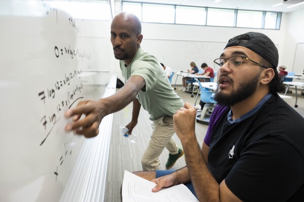 George Mason Term Instructor Ermias Kassaye, left, helps a student figure out an equation during a summer math boot camp on Thursday, Aug. 1, 2023 at George Mason University in Fairfax. Va. Researchers say math learning suffered during the pandemic for various reasons. An intensely hands-on subject, math was hard to translate to virtual classrooms. (AP Photo/Kevin Wolf)