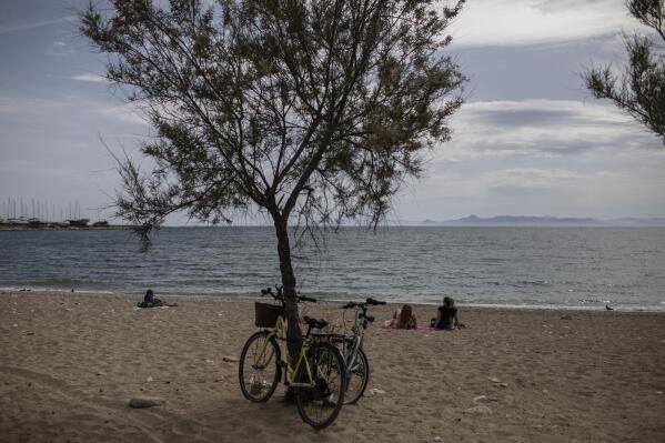 People sit a beach n Alimos, a seaside suburb of Athens, on Friday April 23, 2021. Easter holidays are often celebrated with relatives outside Athens and other cities, but the government has said COVID-19 infection levels remain too high to allow free travel.(AP Photo/Petros Giannakouris)