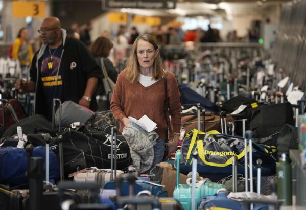 FILE - A traveler wades through a field of unclaimed bags at the Southwest Airlines luggage carousels at Denver International Airport, Dec. 27, 2022, in Denver. With its flights now running on a roughly normal schedule, Southwest Airlines is turning its attention to luring back customers and repairing damage to a reputation for service after canceling 15,000 flights around Christmas. The disruptions started with a winter storm and snowballed when Southwest's ancient crew-scheduling technology failed.(AP Photo/David Zalubowski, File)