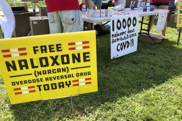 FILE - Signs are displayed at a tent during a health event, June 26, 2021, in Charleston, W.Va. Naloxone is a drug that reverses the effects of an opioid overdose by helping the person breathe again. A federal appeals court asked West Virginia’s highest court Monday, March 18, 2024, to address what constitutes a public nuisance as it reviews a landmark lawsuit against three major U.S. drug distributors. (AP Photo/John Raby, File)