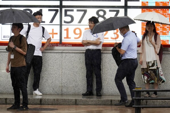 People stand in the rain in front of an electronic stock board showing Japan's Nikkei 225 index at a securities firm Tuesday, Aug. 22, 2023, in Tokyo. (AP Photo/Eugene Hoshiko)