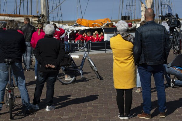 People wait for 25 Dutch teens, center rear, to disembark from the Wylde Swan schooner who sailed home from the Caribbean across the Atlantic when coronavirus lockdowns prevented them flying, at the port of Harlingen, northern Netherlands, Sunday, April 26, 2020. (AP Photo/Peter Dejong)
