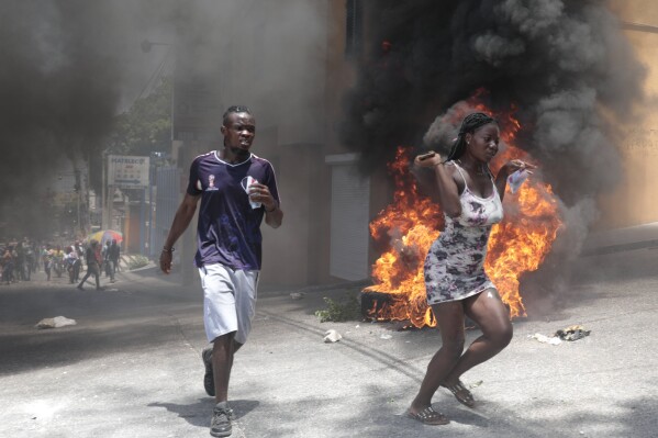 Demonstrators run past tires set on fire during a protest against insecurity in Port-au-Prince, Haiti, Monday, Aug. 7, 2023. (AP Photo/Odelyn Joseph)