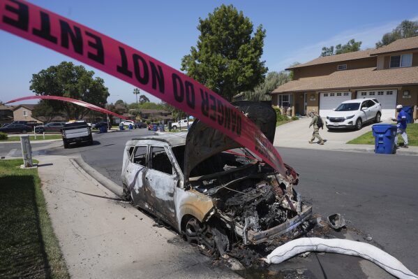 Police tape blows in the wind next to a burned vehicle after a small plane crashed into a San Diego neighborhood earlier in the morning, setting several homes on fire and forcing evacuations along several blocks early Thursday, May 22, 2025. (AP Photo/Gregory Bull)