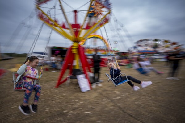 Men enjoy a swing ride at a fair in Hagioaica, Romania, Saturday, Sept. 16, 2023. For many families in poorer areas of the country, Romania's autumn fairs, like the Titu Fair, are one of the very few still affordable entertainment events of the year. (AP Photo/Andreea Alexandru)