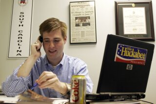 FILE - In this Dec. 28, 2007, file photo, Adam Piper, one of only four full-time staffers for Mike Huckabee's presidential campaign in South Carolina, answers calls and returns emails from the state campaign headquarters in Columbia, S.C. Piper, the executive director of a national group that advocates for Republican attorneys general has resigned in the fallout of a robocall sent out by the association’s political arm urging people to march to the U.S. Capitol last week ahead of the violent assault that followed. The Republican Attorneys General Association and the Rule of Law Defense Fund accepted the voluntary resignation of Piper on Monday, Jan. 11, 2021. (AP Photo/Brett Flashnick, File)